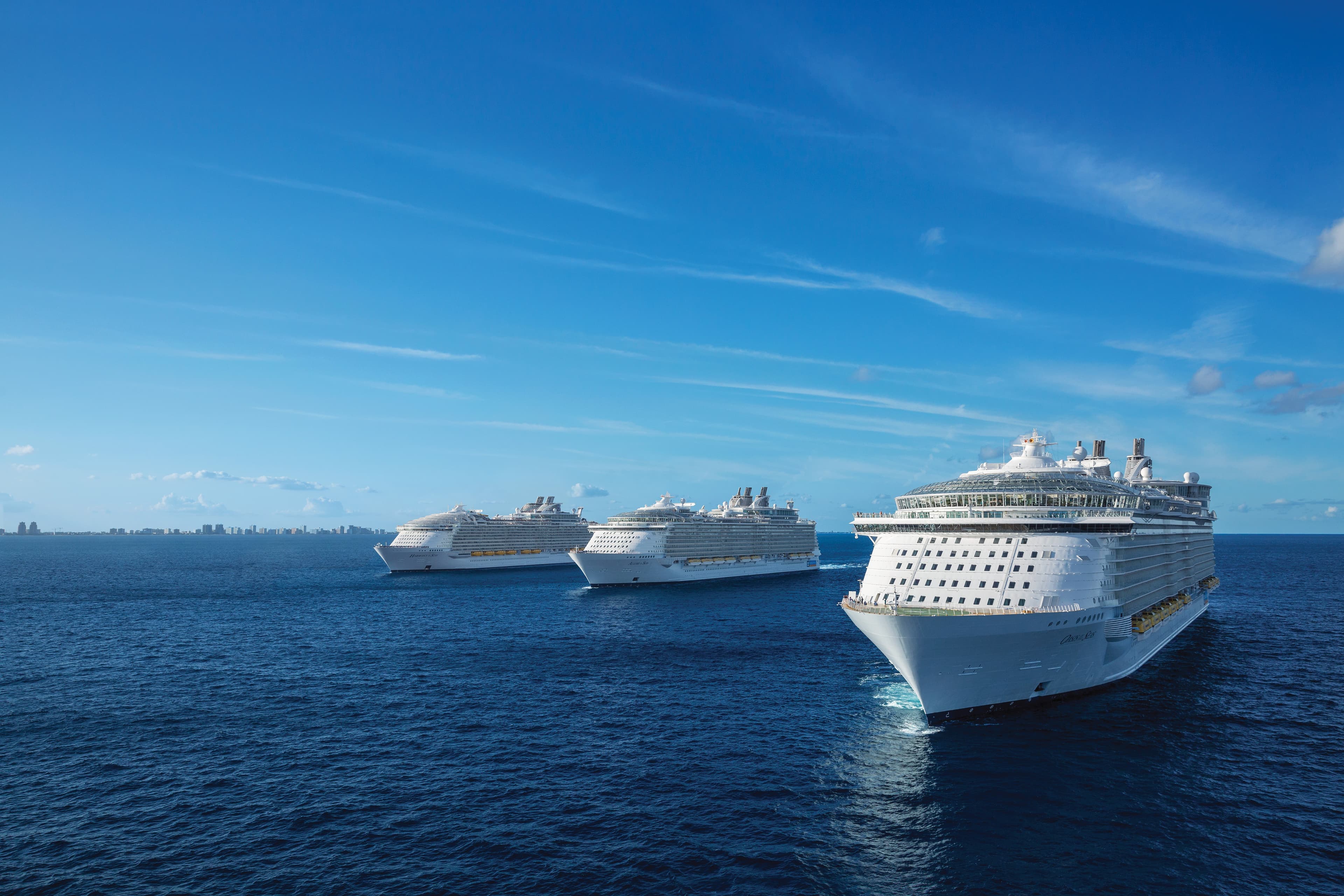 Երեք Royal Caribbean կրուիզային նավեր լողում են շարքով բաց օվկիանոսում՝ պայծառ կապույտ երկնքի տակ: